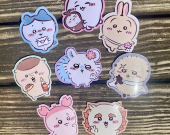 May include: A collection of eight die-cut stickers featuring various cartoon characters with expressive faces. The designs include a blue cat holding a letter, a purple creature with a flower, a tan rabbit, a brown character with a taco, and other whimsical figures.