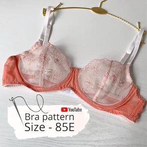 Peut inclure: Un soutien-gorge pêche avec des bretelles blanches et des détails de dentelle florale délicate. Le soutien-gorge est présenté sur un cintre doré. Le texte sur l'image indique "Bra pattern Size - 85E" avec un logo YouTube.