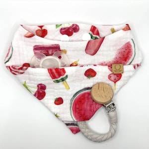 Puede incluir: Babero bandana blanco con un colorido estampado de frutas, que incluye sandía, fresas y cerezas. Cuenta con un mordedor de madera con una correa trenzada gris y un chupete en el bolsillo. El babero tiene dos broches blancos.
