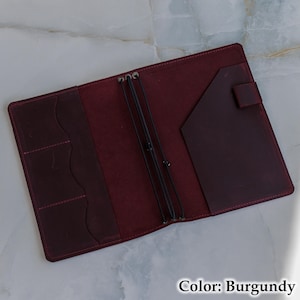May include: Burgundy leather journal, open to reveal pockets and elastic closures. Features a pocket on the right and three card slots on the left. The text "Color: Burgundy" is visible at the bottom of the image.