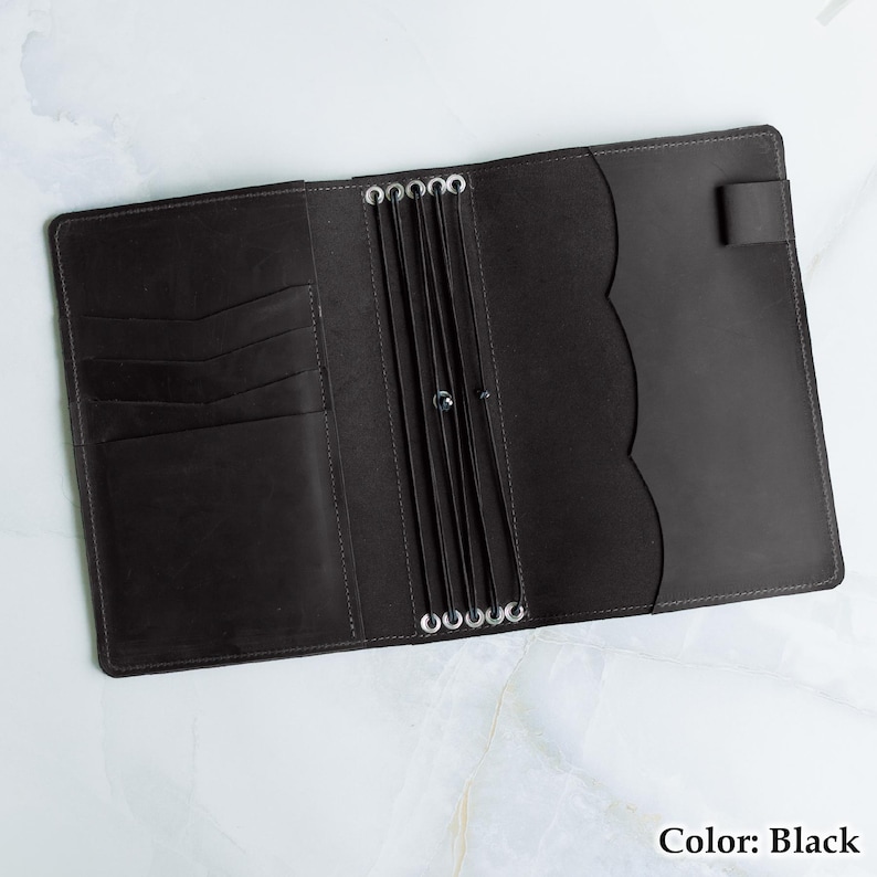 Pu&ograve; includere: Diario in pelle nera aperto con pi&ugrave; fessure per carte e un bordo smerlato. Il diario ha anelli argentati per tenere le pagine e una chiusura con cinturino. Il testo "Color: Black" &egrave; visibile.