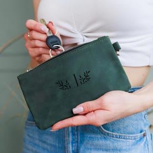 May include: A dark green leather pouch with a zipper closure. The pouch features the letter "J" with a decorative leaf design. A set of keys is attached to the pouch. The pouch is approximately 6 inches long and 4 inches high.