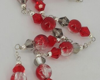 May include: A silver necklace featuring alternating red and clear beads with faceted red and gray crystal accents. The necklace has a delicate chain and a lobster clasp.