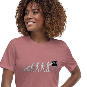 May include: A dusty rose t-shirt featuring a graphic of the evolution of man, culminating in a figure standing before a chalkboard with the equation x^2+1=0. The shirt is made of a soft material.