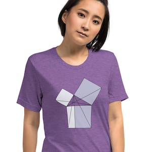 May include: A purple t-shirt featuring a geometric design in shades of gray and white. The graphic appears to be an abstract representation of a box or cube with open sides. The shirt is made of a soft material.