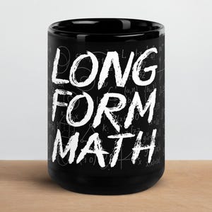 May include: Black ceramic mug with the words "LONG FORM MATH" in white, bold, handwritten-style font. The mug has a background of faint mathematical equations and symbols. The mug is on a wooden surface.