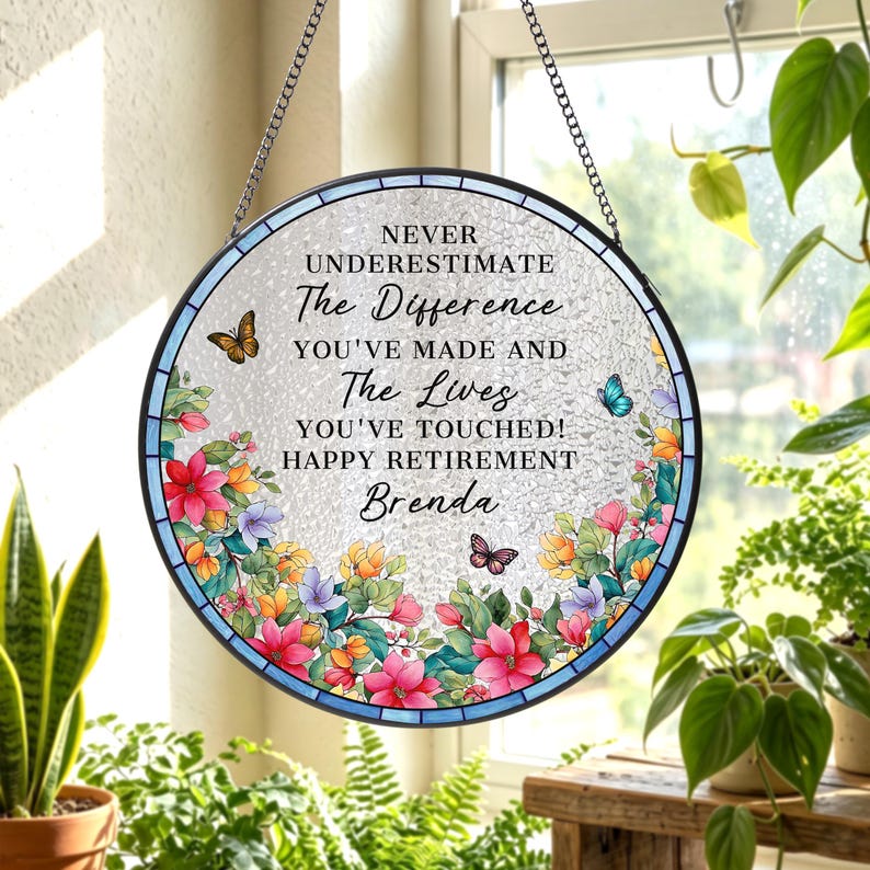 May include: Round, stained-glass window art with a floral border and butterflies. The text reads, "NEVER UNDERESTIMATE The Difference YOU'VE MADE AND The Lives YOU'VE TOUCHED! HAPPY RETIREMENT Brenda."