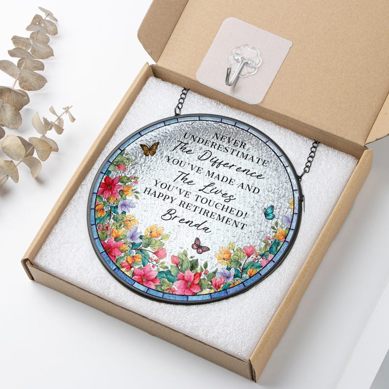 May include: A round, stained-glass retirement gift with a floral border and butterflies. The text reads "Never Underestimate The Difference You've Made and The Lives You've Touched! Happy Retirement Brenda."