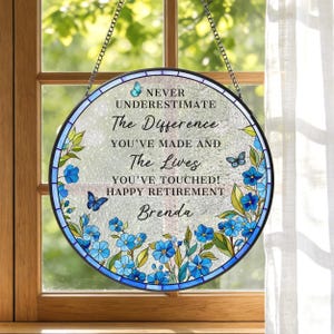 May include: Round stained glass window art with a floral border in shades of blue and green. The text reads "NEVER UNDERESTIMATE The Difference YOU'VE MADE AND The Lives YOU'VE TOUCHED! HAPPY RETIREMENT Brenda."