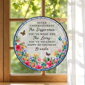 May include: Round, stained glass window art with a floral border and butterflies. The text reads "NEVER UNDERESTIMATE The Difference YOU'VE MADE AND The Lives YOU'VE TOUCHED! HAPPY RETIREMENT Brenda."