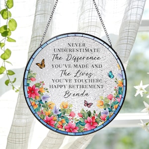 May include: Round stained glass retirement gift with a floral border and butterflies. The text reads "NEVER UNDERESTIMATE The Difference YOU'VE MADE AND The Lives YOU'VE TOUCHED! HAPPY RETIREMENT Brenda."