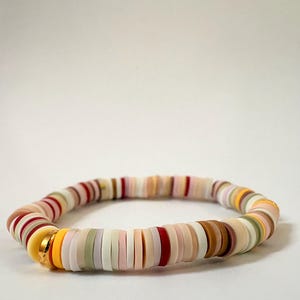 Peut inclure: Un bracelet de perles color&eacute;es avec des perles plates et rondes de diff&eacute;rentes couleurs, dont le rouge, le jaune, le blanc, le rose et le marron. Le bracelet a un fermoir dor&eacute;. Les perles sont enfil&eacute;es pour former une forme circulaire flexible.