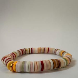 Peut inclure: Un bracelet color&eacute; compos&eacute; de perles plates et rondes de diff&eacute;rentes couleurs, dont blanc, rose, rouge, marron, jaune et vert. Le bracelet comporte une perle d'accent dor&eacute;e. Les perles sont enfil&eacute;es pour former un bracelet souple.
