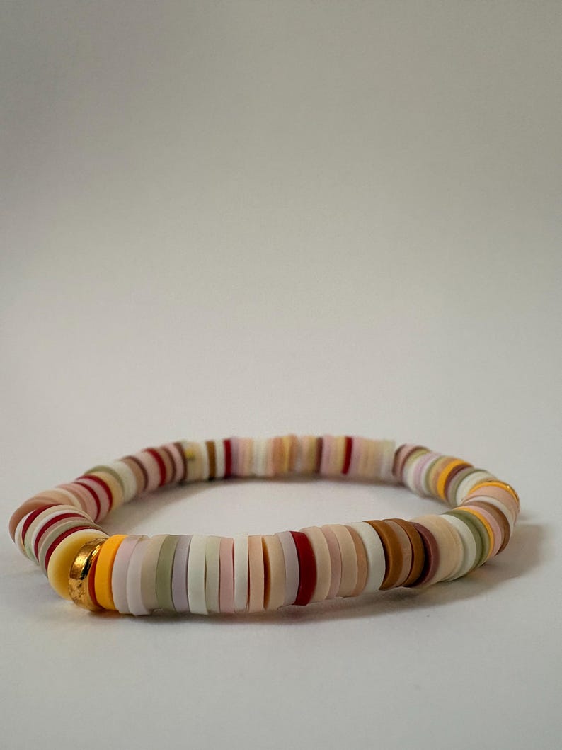 Peut inclure: Un bracelet color&eacute; compos&eacute; de perles plates et rondes de diff&eacute;rentes couleurs, dont blanc, rose, rouge, marron, jaune et vert. Le bracelet comporte une perle d'accent dor&eacute;e. Les perles sont enfil&eacute;es pour former un bracelet souple.