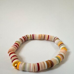 Peut inclure: Un bracelet de perles color&eacute;es avec des perles plates et rondes de diff&eacute;rentes nuances de rose, rouge, jaune, marron et vert. Le bracelet est assembl&eacute; avec un fermoir dor&eacute;. Le bracelet mesure environ 18 cm de circonf&eacute;rence.