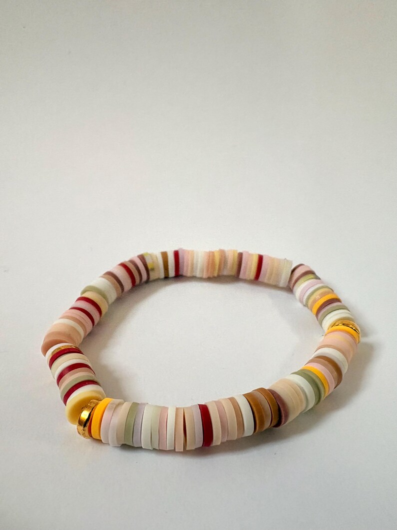 Peut inclure: Un bracelet de perles color&eacute;es avec des perles plates et rondes de diff&eacute;rentes nuances de rose, rouge, jaune, marron et vert. Le bracelet est assembl&eacute; avec un fermoir dor&eacute;. Le bracelet mesure environ 18 cm de circonf&eacute;rence.