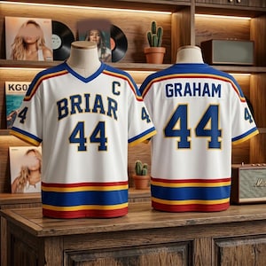 Könnte beinhalten: Ein weißes Eishockeytrikot mit blauen und roten Akzenten, das vorne den Namen BRIAR und die Nummer 44 sowie hinten den Namen GRAHAM und die Nummer 44 zeigt. Das Trikot hat einen V-Ausschnitt sowie blaue und rote Streifen an Ärmeln und Saum.