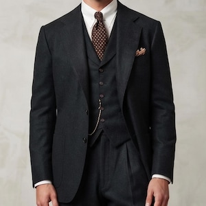 May include: A charcoal three-piece suit consisting of a blazer, a buttoned vest, and pleated trousers. The outfit includes a white collared shirt, a dark brown patterned tie, a pocket square, a gold pocket watch chain, and a straw boater hat.