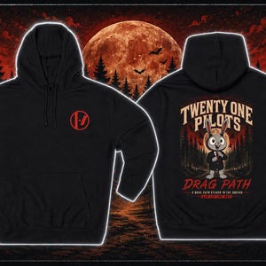 May include: Black hoodie featuring a red logo on the front and a graphic on the back with the text "Twenty One Pilots" and a cartoon rabbit. The background includes a forest, a full moon, and bats.