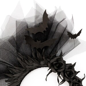 May include: A black Halloween headpiece featuring a black tulle veil, black paper bats, and black roses. The headpiece has a circular base with black leaves and three black roses. The bats are in various sizes and positions.