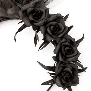 May include: A decorative floral headpiece featuring a series of black roses and leaves. The roses are clustered together, with a dark, matte finish. The headpiece is set against a white background.