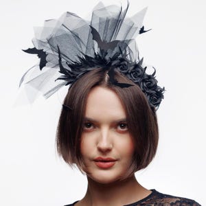 May include: A black headband featuring a cluster of dark roses and layered tulle fabric. The headpiece is adorned with several black bat-shaped cutouts attached to the tulle and the base, creating a layered, textured appearance across the top.