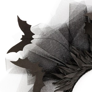 May include: A black Halloween headpiece featuring bat silhouettes and layered black tulle. The headpiece also includes black feathers. The design is set against a white background, highlighting the dark colors and intricate details.