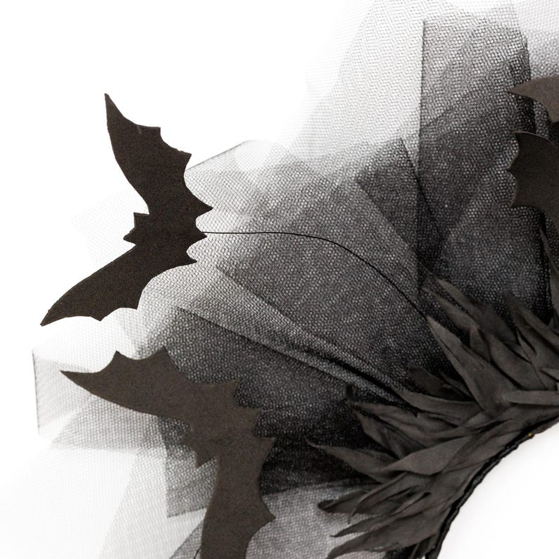 May include: A black Halloween headpiece featuring bat silhouettes and layered black tulle. The headpiece also includes black feathers. The design is set against a white background, highlighting the dark colors and intricate details.