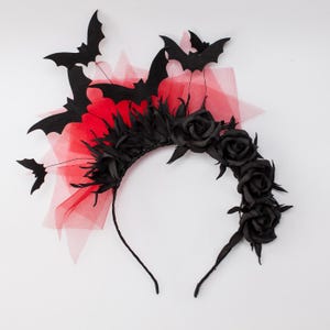 May include: A black headband with a Halloween theme. The headband features black bat silhouettes, black roses, and red tulle. The design is a combination of gothic and festive elements, perfect for a costume or themed event.