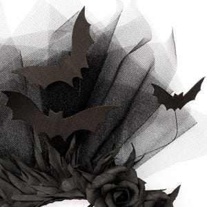 May include: A black Halloween-themed headpiece featuring felt bat cutouts, black tulle, and a black rose. The headpiece has a layered design with the bats seemingly flying above the tulle. The overall aesthetic is dark and gothic.