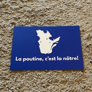 May include: A blue rectangular card with a white outline of the Quebec province. The text "La poutine, c'est la nôtre!" is printed in white. The card is resting on a textured, light brown surface.