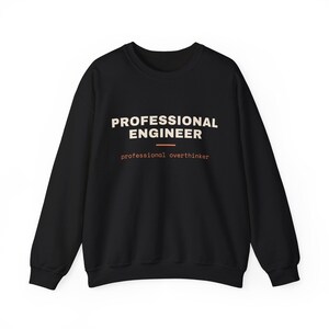 May include: A black long-sleeve sweatshirt featuring the text "PROFESSIONAL ENGINEER" in large cream-colored letters, followed by a horizontal orange line and the smaller orange text "professional overthinker" centered on the chest.