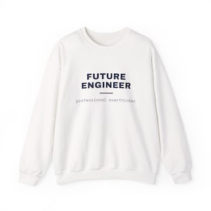 Puede incluir: Una sudadera blanca de manga larga con cuello redondo que presenta el texto FUTURE ENGINEER en letras mayúsculas azul oscuro, una línea horizontal y el texto professional overthinker en una fuente pequeña.