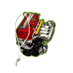 May include: A green, engine-shaped air freshener with a white string for hanging. The engine illustration features red, silver, yellow, and black details. The air freshener is designed to resemble a car engine.
