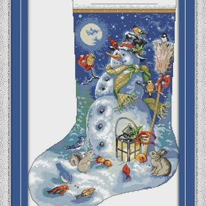 May include: Cross-stitch design of a snowman in a winter scene, framed in blue. The snowman wears a hat and scarf, surrounded by birds, a squirrel, and a rabbit. A lantern and apples are also present.