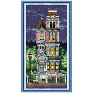 May include: A cross-stitch pattern of a Victorian house with a blue frame. The house is pink, blue, and brown with lit windows, a black cat, and a starry night sky. A black cat is on the front porch. A black wrought iron fence and a street lamp are in the foreground.