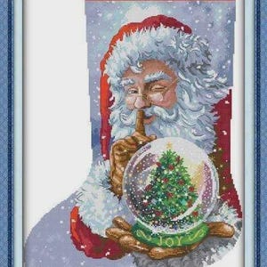 Op de afbeelding: Kruissteek kerstsok met een knipogende kerstman die een sneeuwbol vasthoudt met een kerstboom erin. De sneeuwbol staat op een groene basis met het woord "JOY". De achtergrond is een besneeuwde scène.
