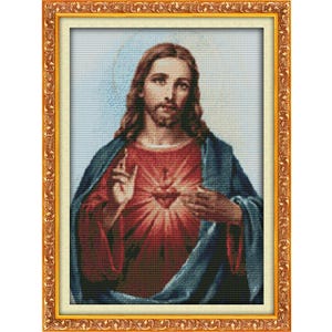 Puede incluir: Un retrato en punto de cruz enmarcado de Jesucristo. La obra de arte presenta a Jesús con cabello castaño largo, barba y una túnica roja con un corazón brillante. El marco es dorado con detalles ornamentados.