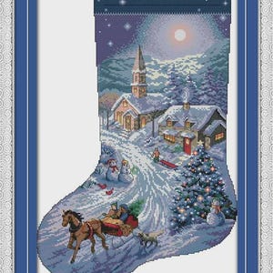 May include: A cross-stitch Christmas stocking design featuring a winter village scene. A horse-drawn sleigh travels down a snowy road past a church, houses, snowmen, and a decorated Christmas tree under a full moon. The stocking is framed in blue.