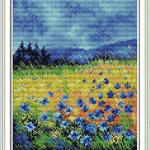May include: A framed cross-stitch landscape depicting a field of blue flowers and tall grasses beneath a cloudy blue sky. The artwork has a pixelated look, with a dark forest silhouette in the background.