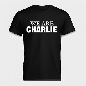 May include: Black t-shirt with the white text "WE ARE CHARLIE" printed across the chest. The shirt has short sleeves and a crew neck. The text is in a bold, sans-serif font.