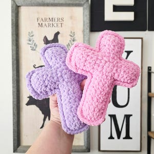 Puede incluir: Dos objetos de peluche con forma de cruz hechos de hilo suave y texturizado. Una cruz es de color morado claro y la otra es de color rosa claro. Ambos art&iacute;culos presentan una construcci&oacute;n gruesa y redondeada con un patr&oacute;n de tejido esponjoso.