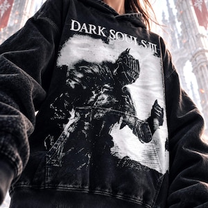 Könnte beinhalten: Ein schwarzer Kapuzenpullover in Acid-Wash-Optik mit einem großen weißen Grafikdruck eines Ritters in Rüstung. Der Text "DARK SOULS III" ist in Weiß über dem Ritter aufgedruckt. Der Hoodie verfügt über eine Kängurutasche und gerippte Bündchen.