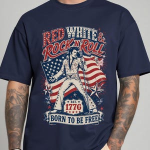 May include: Navy blue t-shirt featuring a graphic of a singer with an American flag and the text "RED WHITE & ROCK N ROLL". The graphic also includes the text "EST. 1776" and "BORN TO BE FREE".