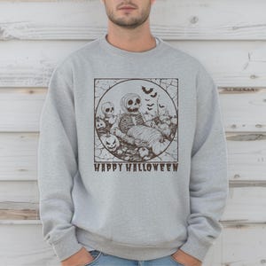 Könnte beinhalten: Hellgraues Sweatshirt mit einem Halloween-Motiv. Die Grafik zeigt ein Skelett, Kürbisse, Fledermäuse und die Worte "HAPPY HALLOWEEN" in einem Kreis. Das Sweatshirt ist aus weichem Material.