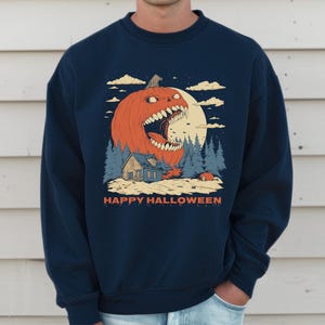 May include: Navy blue sweatshirt featuring a Halloween-themed graphic. The design includes a large orange pumpkin with an open mouth, a house, trees, and the text "HAPPY HALLOWEEN". The artwork is set against a full moon and cloudy sky.