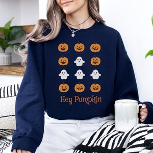 Op de afbeelding: Marineblauwe sweatshirt met een patroon van oranje pompoenen en witte geesten. De tekst "Hey Pumpkin" is in oranje gedrukt. Een casual kledingstuk voor het herfstseizoen.
