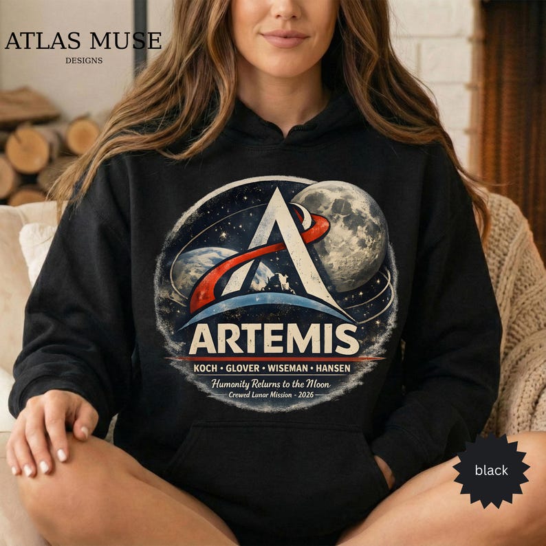 May include: Black hooded sweatshirt featuring the Artemis logo with a stylized A, planets, and the moon. The design includes the text "ARTEMIS" and "Humanity Returns to the Moon - 2026". The sweatshirt has a kangaroo pocket.