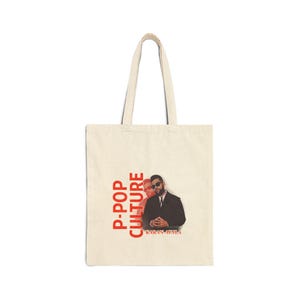 May include: Cream-colored tote bag with a rectangular design. The bag features the words "P-POP CULTURE" in red, stacked vertically on the left side. Below the text is a picture of two people, and the name "KARAN AUJLA" is printed below the image.