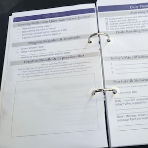 Può includere: Diario giornaliero aperto con interno bianco, con sezioni per la tenuta del diario, la riflessione e la definizione degli obiettivi. Include suggerimenti per le riflessioni serali, gli snapshot dei progressi e l'espressione creativa. L'agenda è tenuta insieme da anelli di metallo argentato.